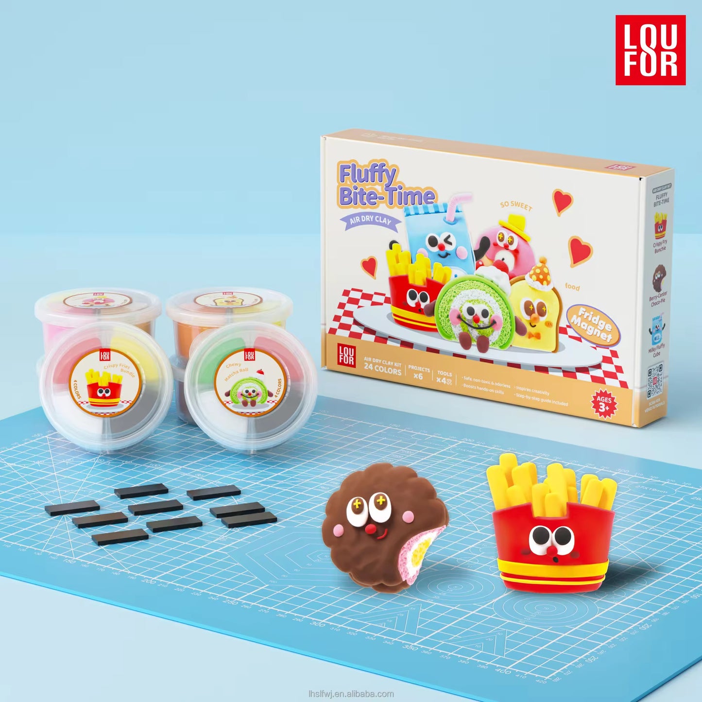 A children's craft kit labeled 'Fluffy Bite-Time' by LOU FOR, shown with its box, two small plastic containers of colorful dough, several black rectangular pieces, and two finished character-shaped items on a blue gridded mat against a light blue background.
